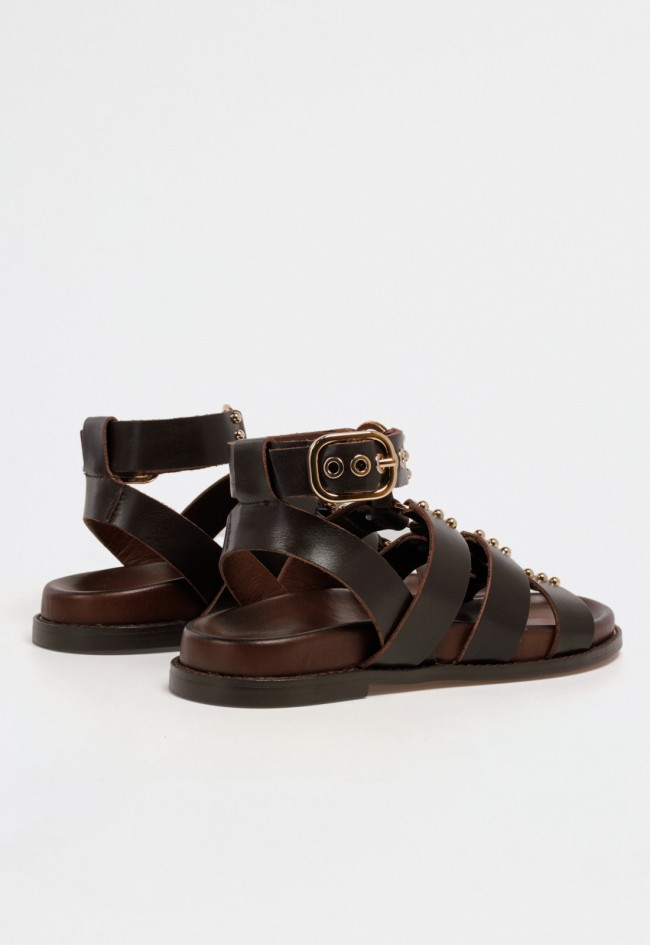 Sandalia plana de mujer estilo romana en piel marrón con tachuelas doradas y cierre al tobillo con hebilla VAS d51013